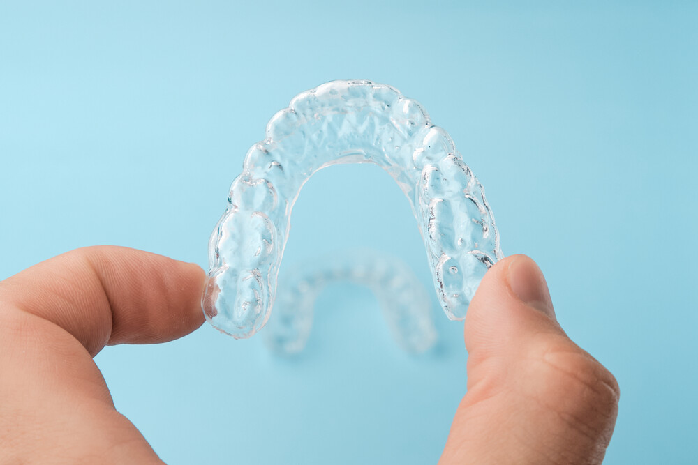 Close up mans hand holding invisible aligners for whitening and straightening of teeth on the blue background. Orthodontic therapy after brackets. Teeth healthcare.